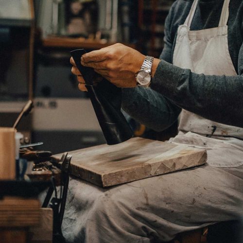Le mani del calzolaio tengono una scarpa sulle ginocchia, accanto alla pietra per battere il cuoio